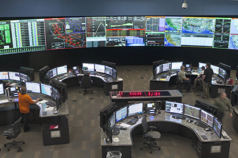 A large room with a wall of electronic displays and managers seated at computers