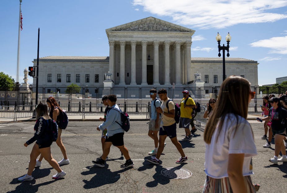 About a dozen teenagers, many with backpacks, walk past the U.S. Supreme Court.