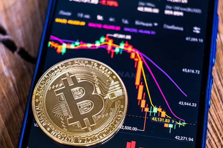 Bitcoin coin on the background of a smartphone screen with a graph of fall of cryptocurrency market on the Binance exchange.