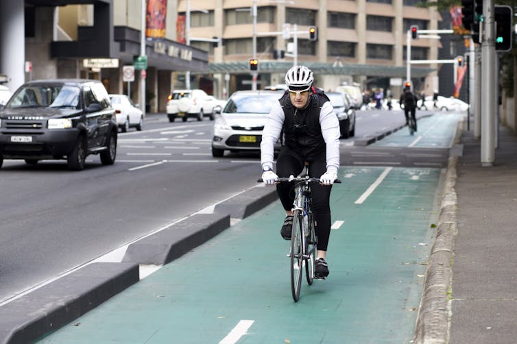 Man cycling in bike lane along a busy road