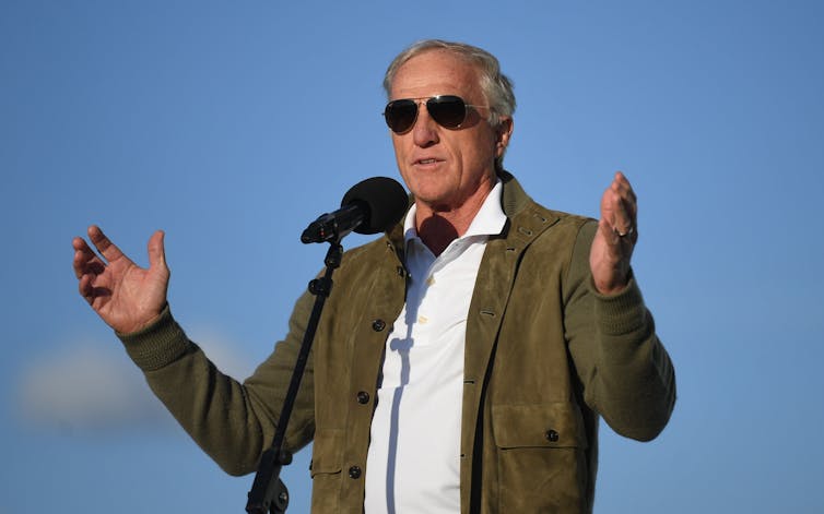 A close up shot of Greg Norman with sunglasses while delivering a speech