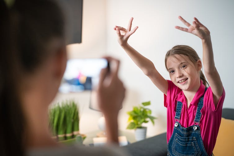 Young girl poses as her mother takes a video on her mobile phone
