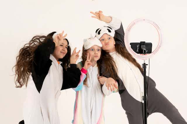 Three children in costume ham it up in front of a camera phone and ringlight