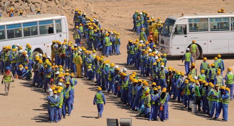 Many migrant construction workers queue up for the bus back to their accommodation camp