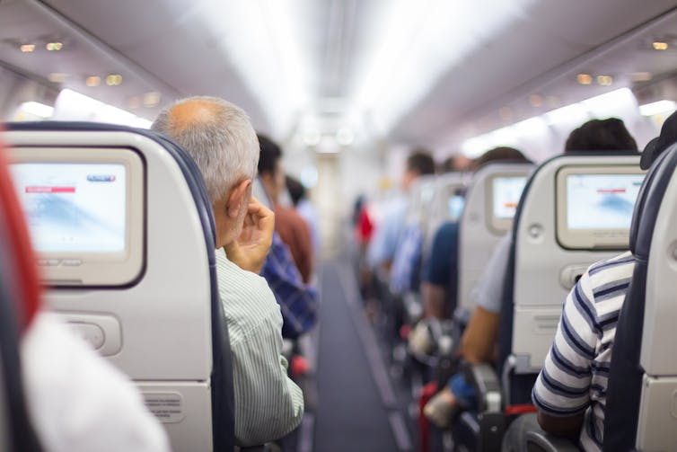 People seated on an aeroplane viewed from the central back aisle