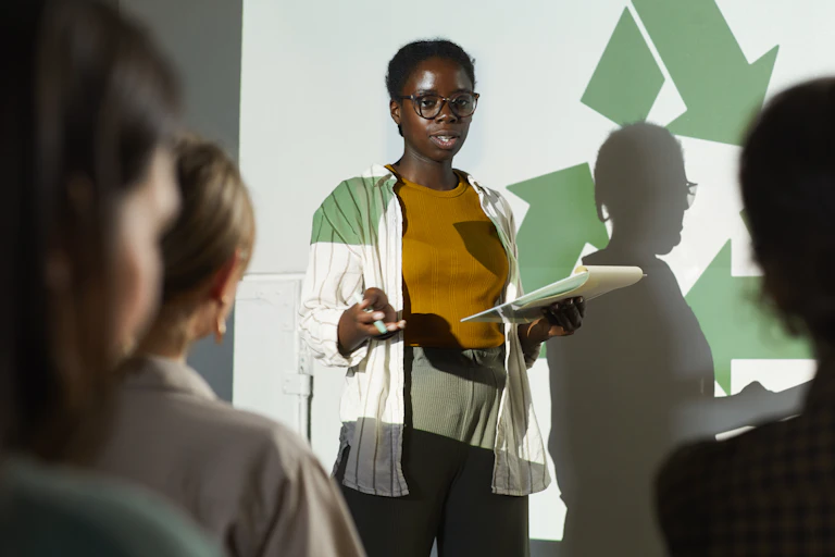 A person stands in front of a green recycling sign speaking to an audience