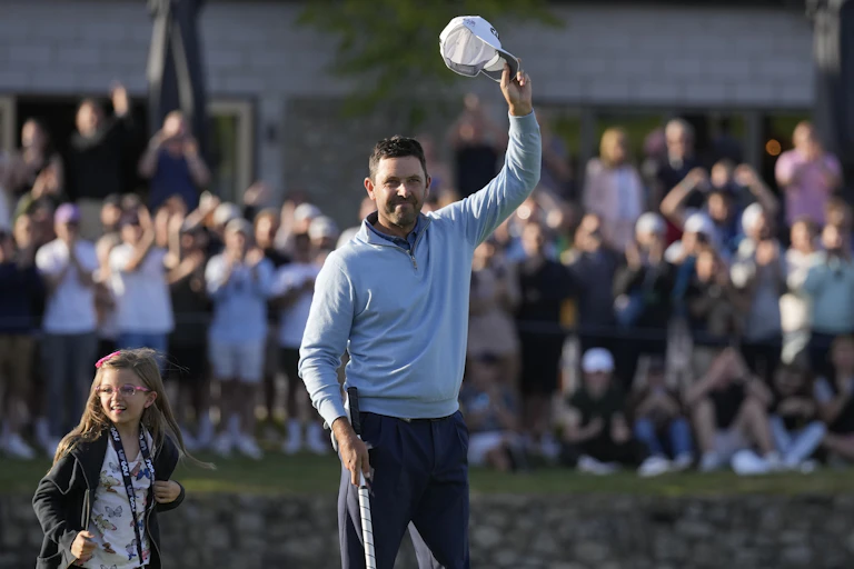 A man holds his hat in the air as fans cheer behind