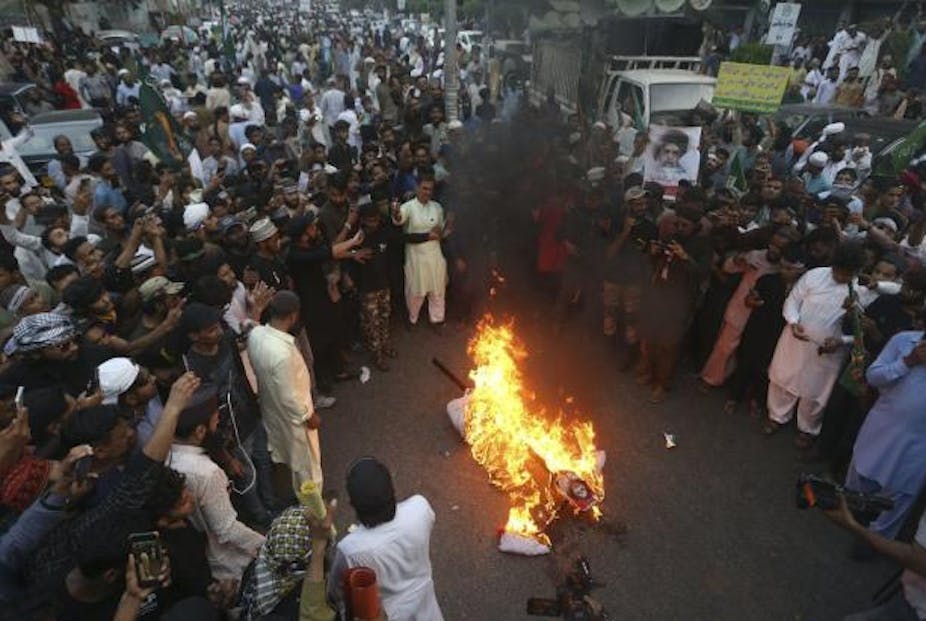 Kerumunan besar berkumpul di sekitar patung yang terbakar selama demonstrasi.