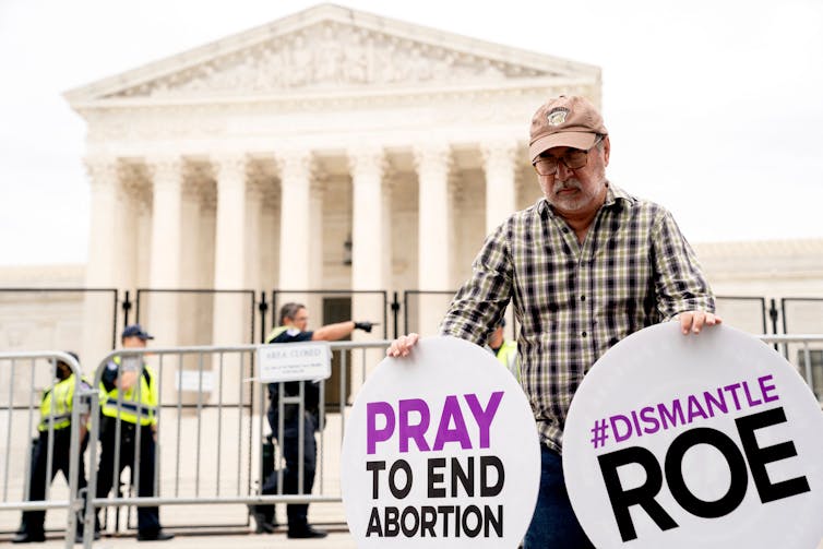 A man holds a sign that says pray to end abortion and dismantle Roe outside the gated Supreme Court