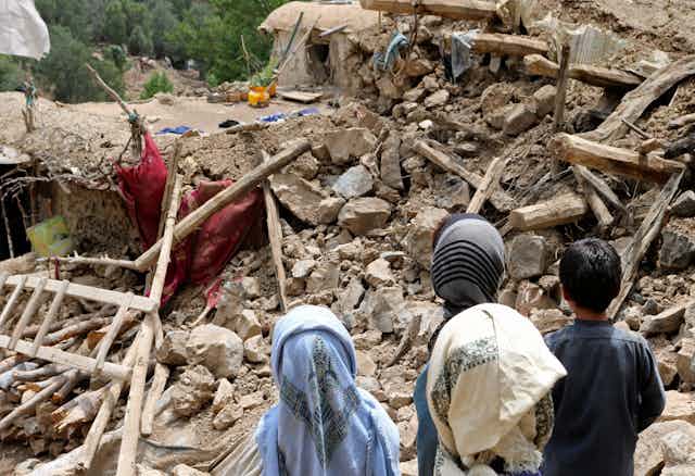 Afghan children stand near rubble.