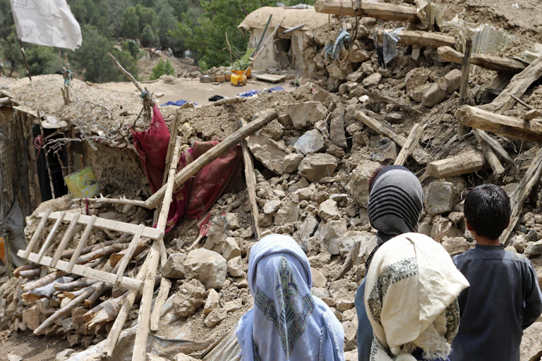 Afghan children stand near rubble.