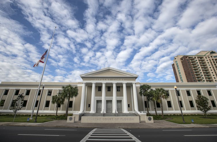 A large court building is shown in front of blue skies with pillowy clouds