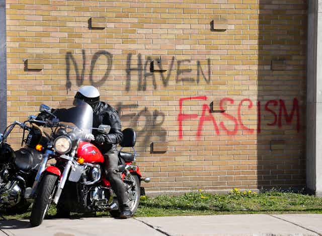 A motorcycle sits in front of graffiti that reads 'no haven for fascism'