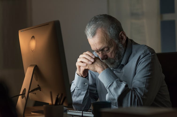 An elderly man sits in front of his laptop looking disappointed