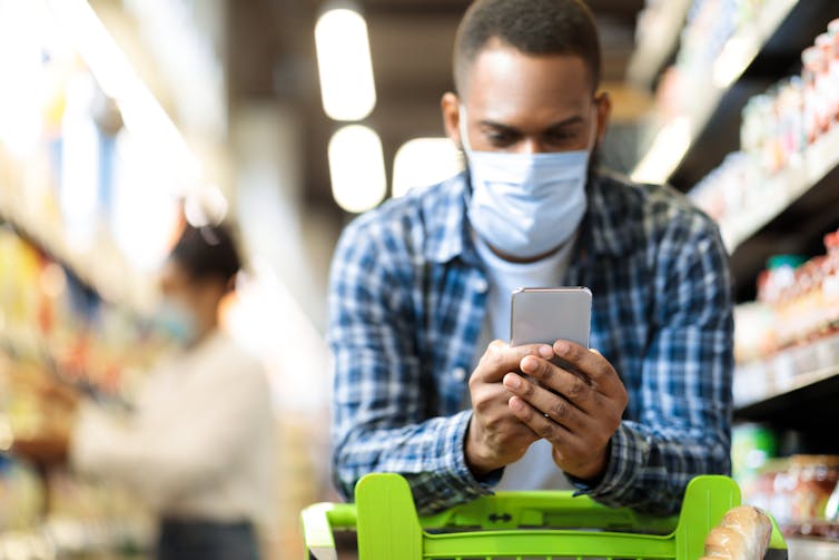 Man in mask looks at phone while shopping in the supermarket.