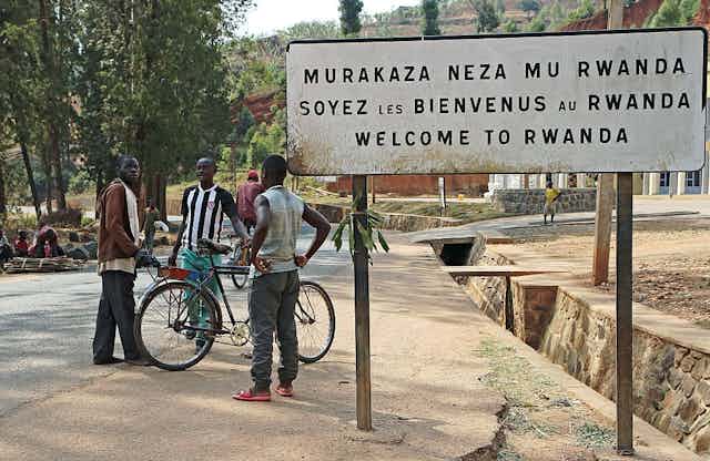 People stand by a placard reading "Welcome to Rwanda" in Akanyaru on the Rwandan side of the street located at the border with Burundi.