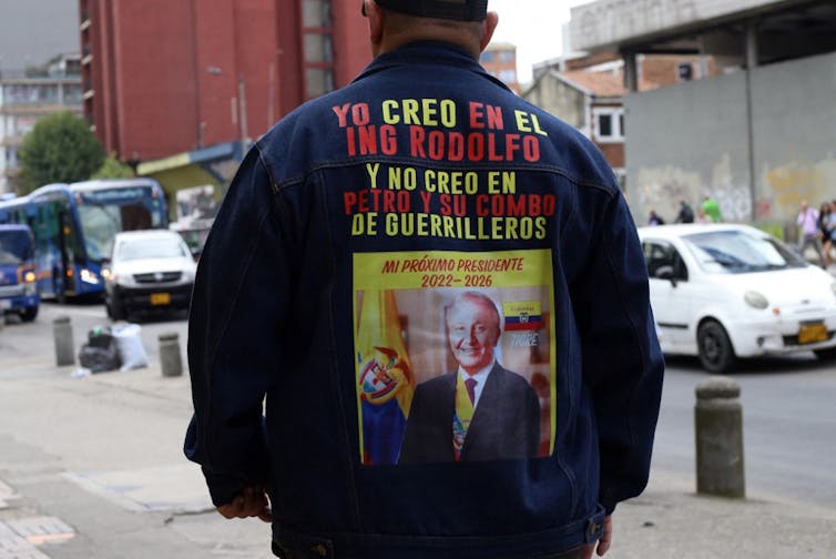 Homme de dos portant une veste sur laquelle il est écrit « Je crois en l’ingénieur Rodolfo et je ne crois pas en Petro et son groupe de guérilleros »