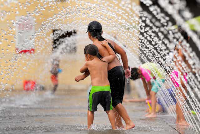 Two children with long braids play in plumes of water.