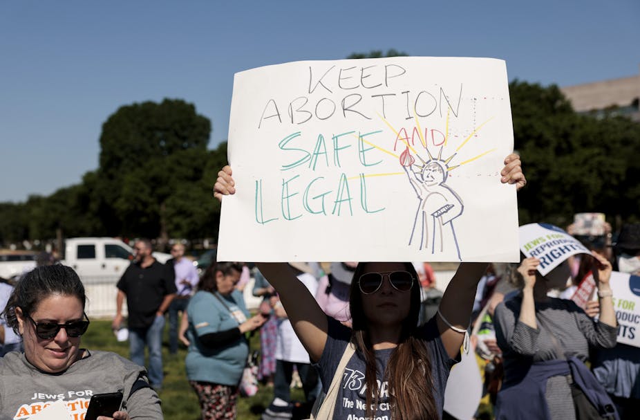 A protester holds aloft a sign with a cartoon of the Statue of Liberty and the words 'Keep Abortion Safe and Legal.'