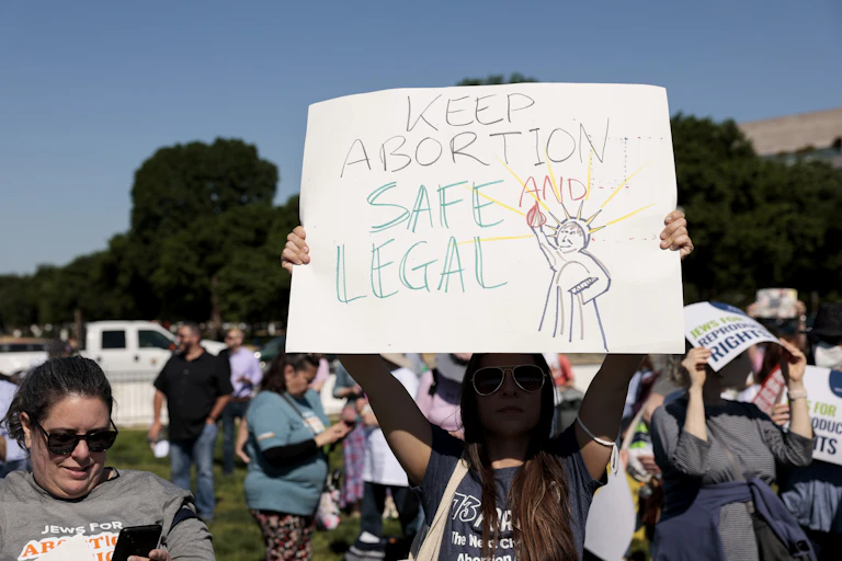 A protester holds aloft a sign with a cartoon of the Statue of Liberty and the words 'Keep Abortion Safe and Legal.'