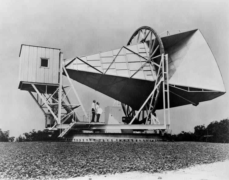 Black and white photo of antenna equipment standing on it by two men