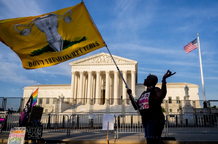 A woman stands outside the Supreme Court holding a flag with a drawing of a uterus on it with the slogan 'Don't tread on my uterus.'