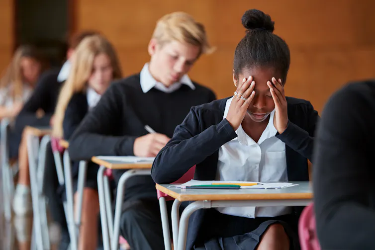 A girl at a desk puts her hands over her head