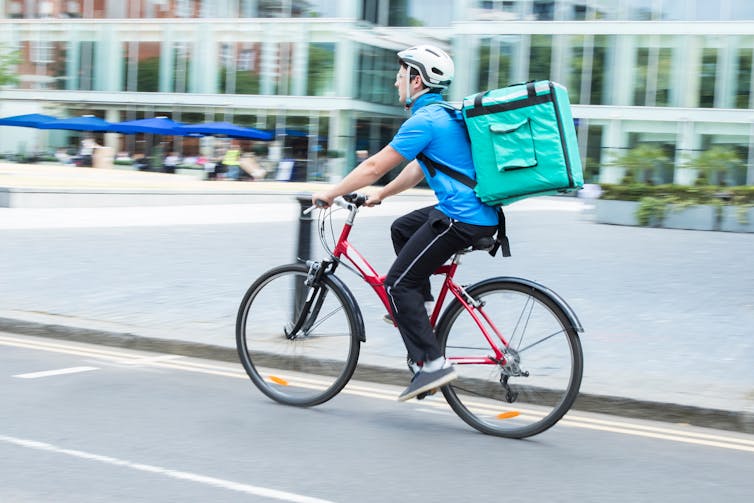 A delivery cyclist on his bike with a delivery box on his back.