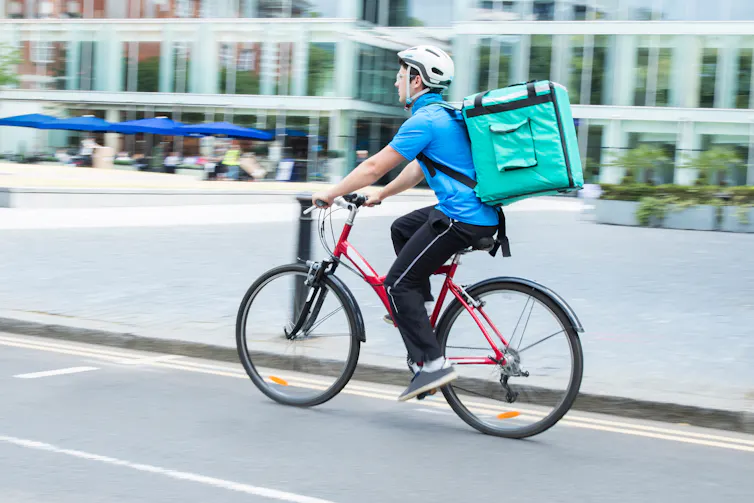 A delivery cyclist on his bike with a delivery box on his back.