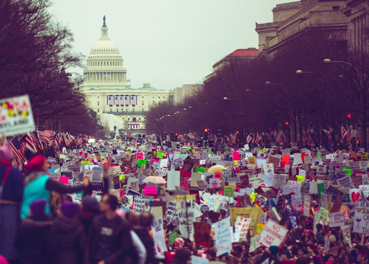 A crowd with colourful banners fill a wide route.