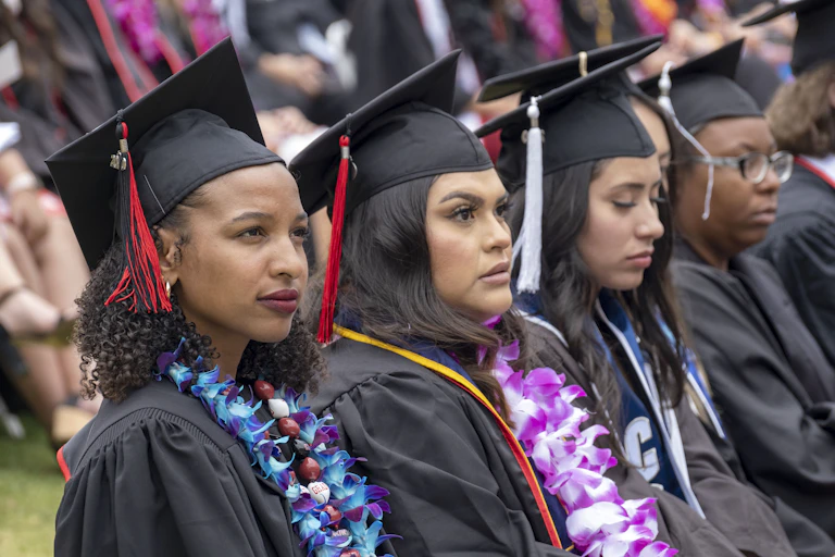 Students in caps and gowns look onward at a graduation ceremony.