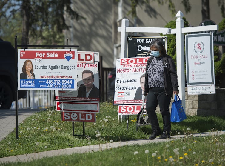 A woman walking past a row of real estate listing signs on a lawn
