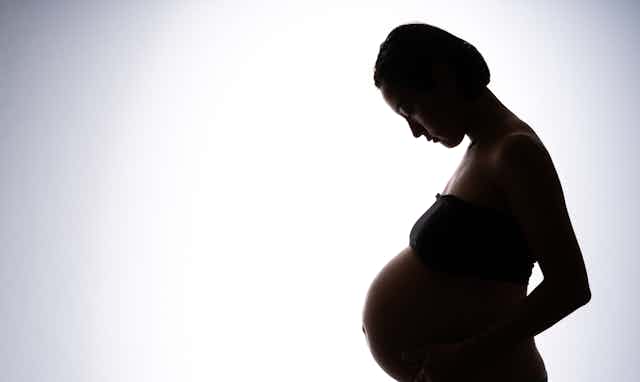 A photograph of a pregnant woman in silhouette against a white background.