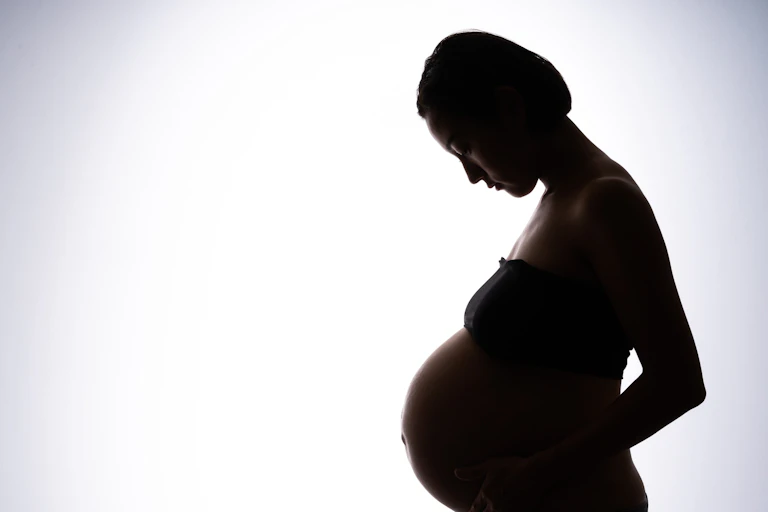 A photograph of a pregnant woman in silhouette against a white background.