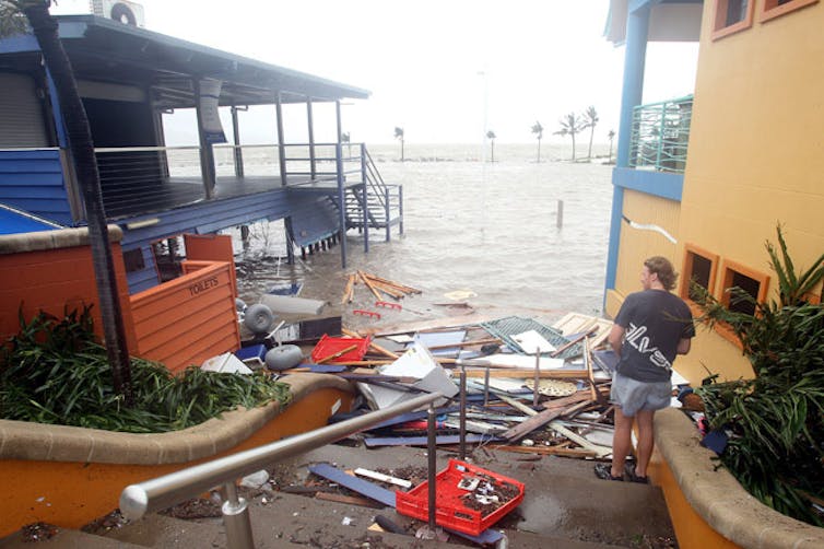 A man looking at debris from cyclone between two beach houses