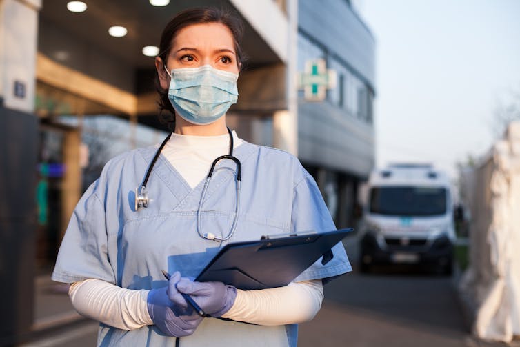 Medical professional with clipboard, stethoscope, mask, outside hopsital.