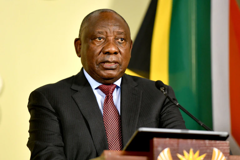 A man wearing a tie and jacket speaks into a microphone at a podium.