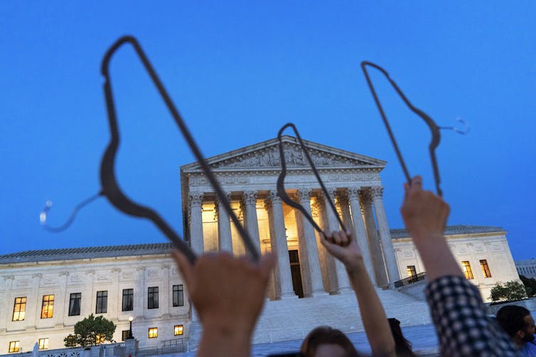 Demonstrators Hold Hangers In The Air Against The Backdrop Of The Supreme Court Building At Dusk.