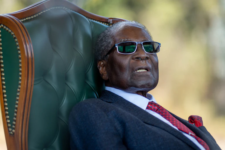 An old man with thinning hair sits on a leather chair.
