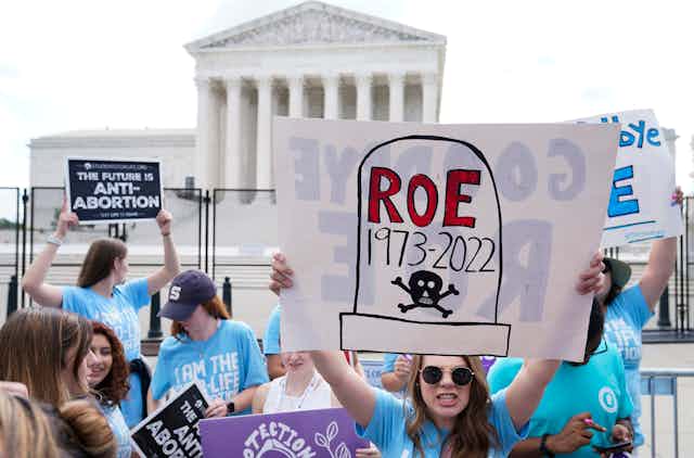 A protester holds up a sign that shows a tombstone with the words Roe 1973-2002