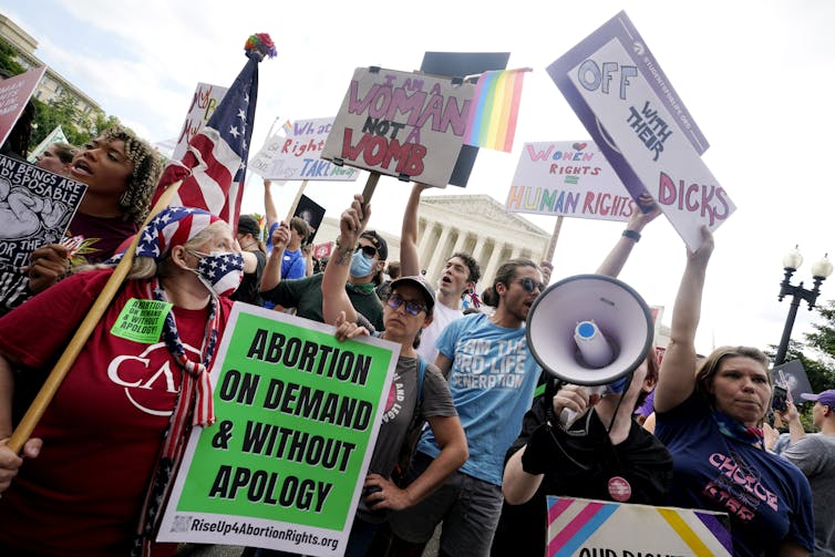 Dozens of protesters hold  signs and bullhorns as the U.S. Supreme Court building can be seen in the background