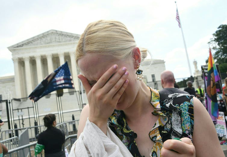 A white, blond woman covers her face with her hand outside the US Supreme Court
