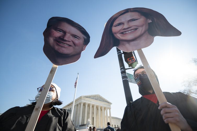Protestors hold up large cut out photos of Brett Kavanaugh and Amy Coney Barrett's heads outside the Supreme Court
