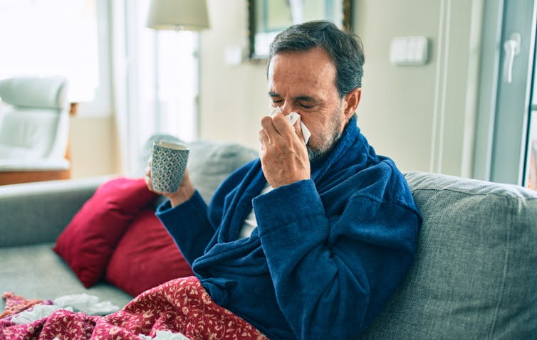 A man blows his nose on the sofa.