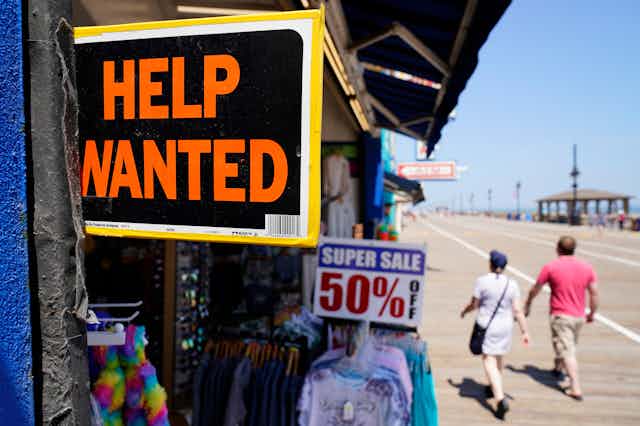 A 'Help Wanted' sign is displayed in a shop along a beach boardwalk