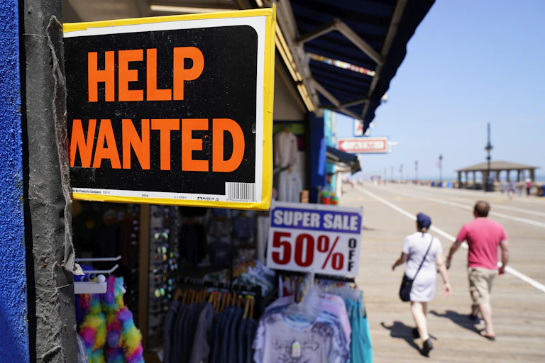 A 'Help Wanted' sign is displayed in a shop along a beach boardwalk