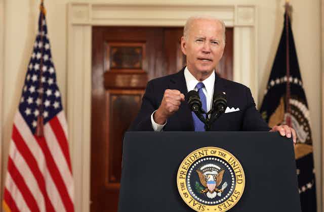 President Joe Biden clenches his fist while speaking behind a podium flanked by flags.