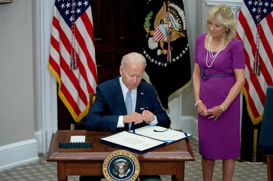President Joe Biden sits at a desk, pen in hand.