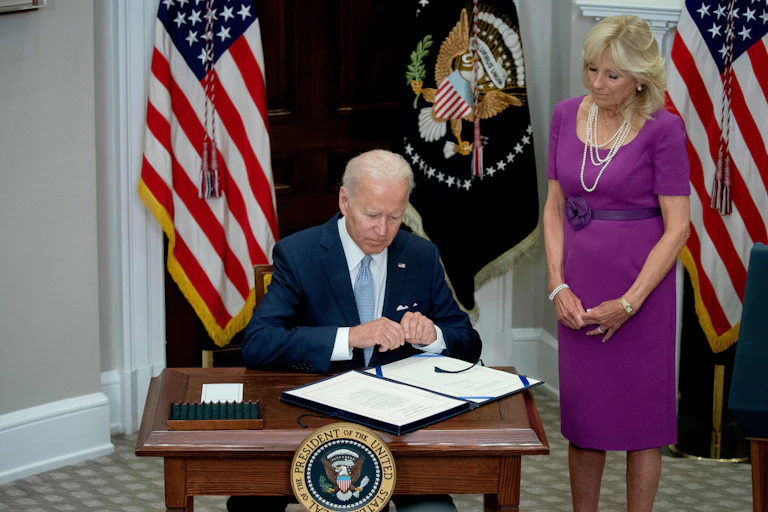 President Joe Biden sits at a desk, pen in hand.