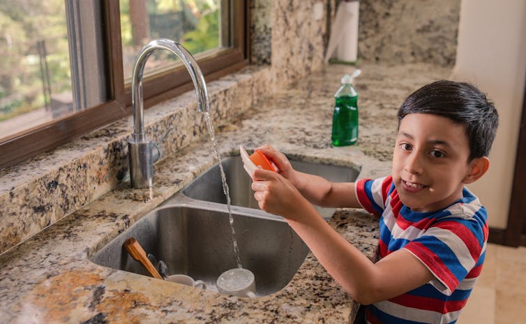 (A child seen washing dishes)